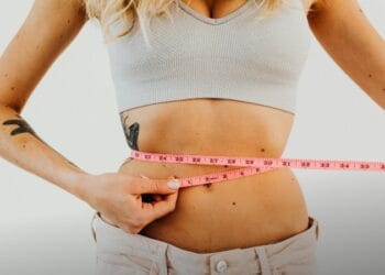 Close-up of woman in sports bra measuring waist with pink tape for fitness goals., tags: weight-loss - pexel