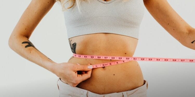Close-up of woman in sports bra measuring waist with pink tape for fitness goals., tags: weight-loss - pexel
