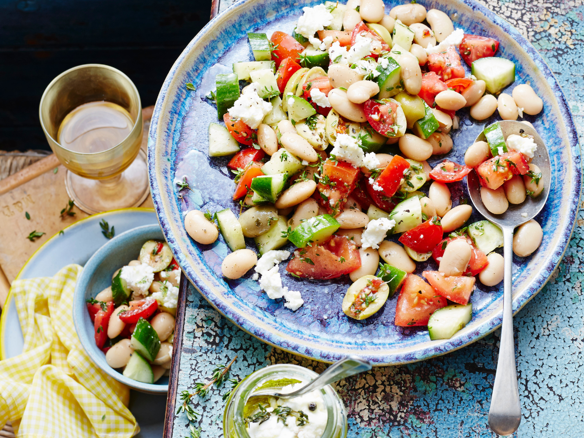 A bowl of giant butter bean and tomato salad, featuring creamy white butter beans mixed with ripe red cherry tomatoes, sliced red onion, fresh herbs, and a light dressing, served in a rustic bowl.