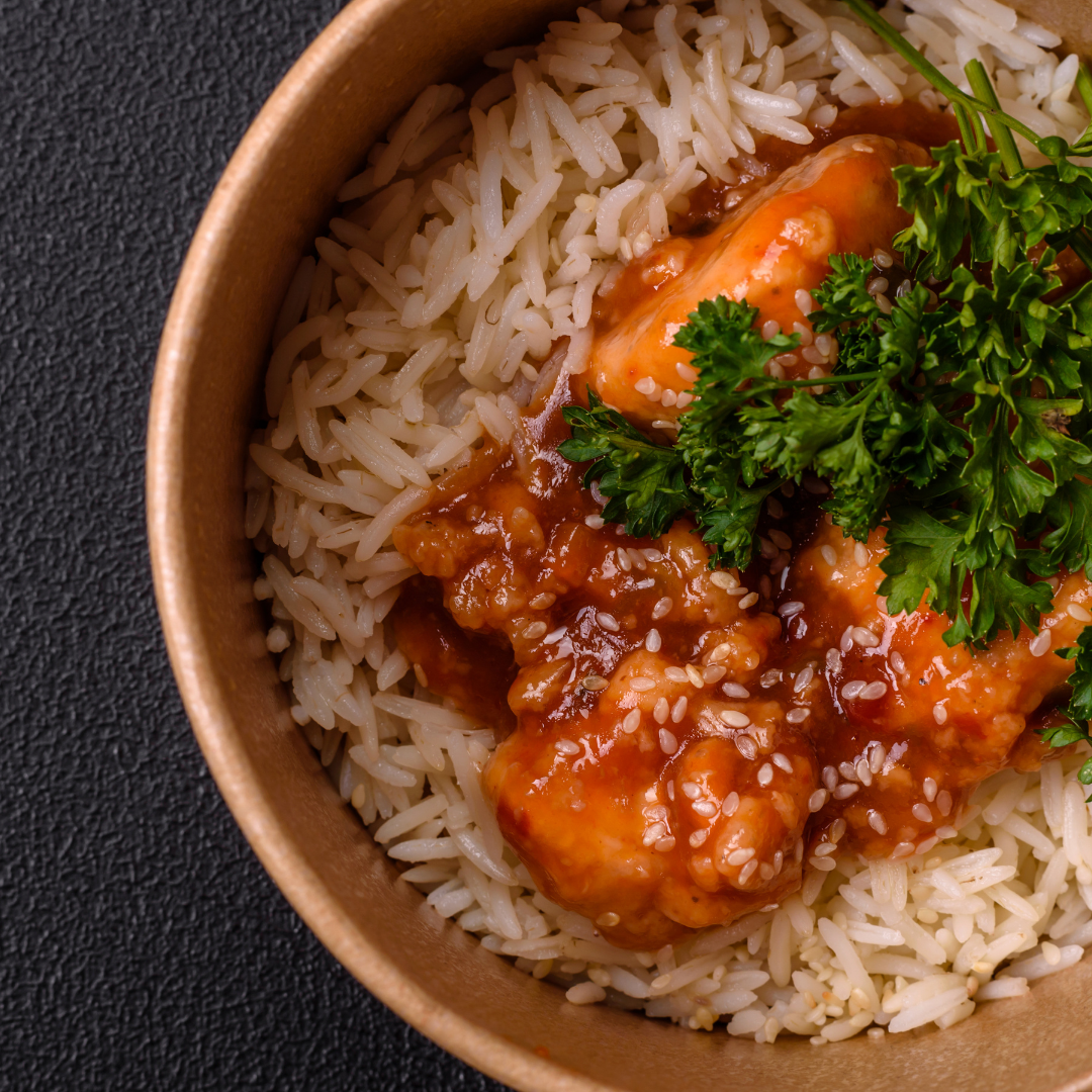 A bowl of rice topped with chicken and herbs with a light sauce